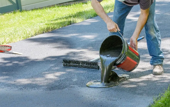 man pouring blacktop sealing on driveway